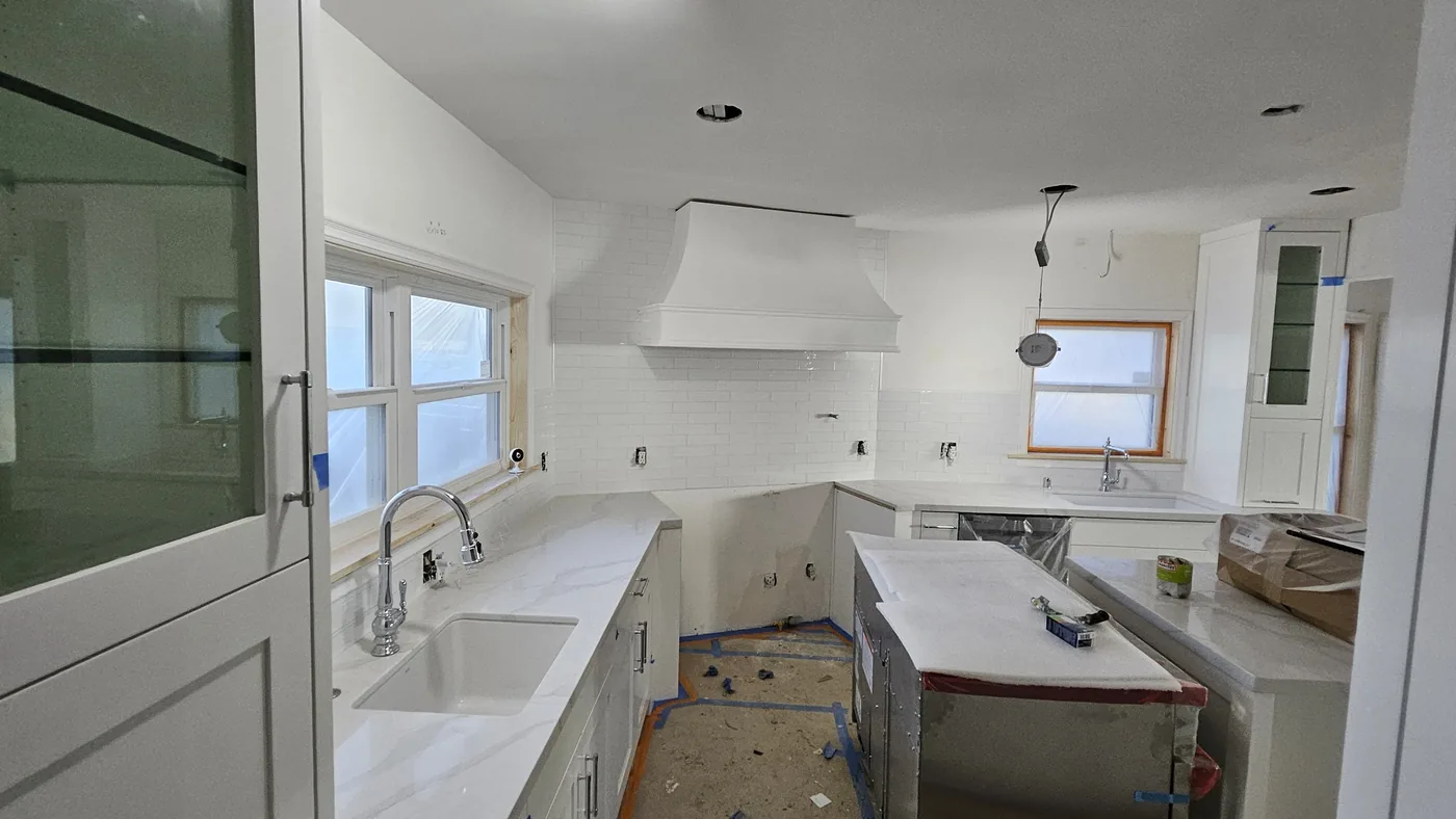 A kitchen mid installation, with stone counters and a white subway backsplash set and the appliances still wrapped in plastic