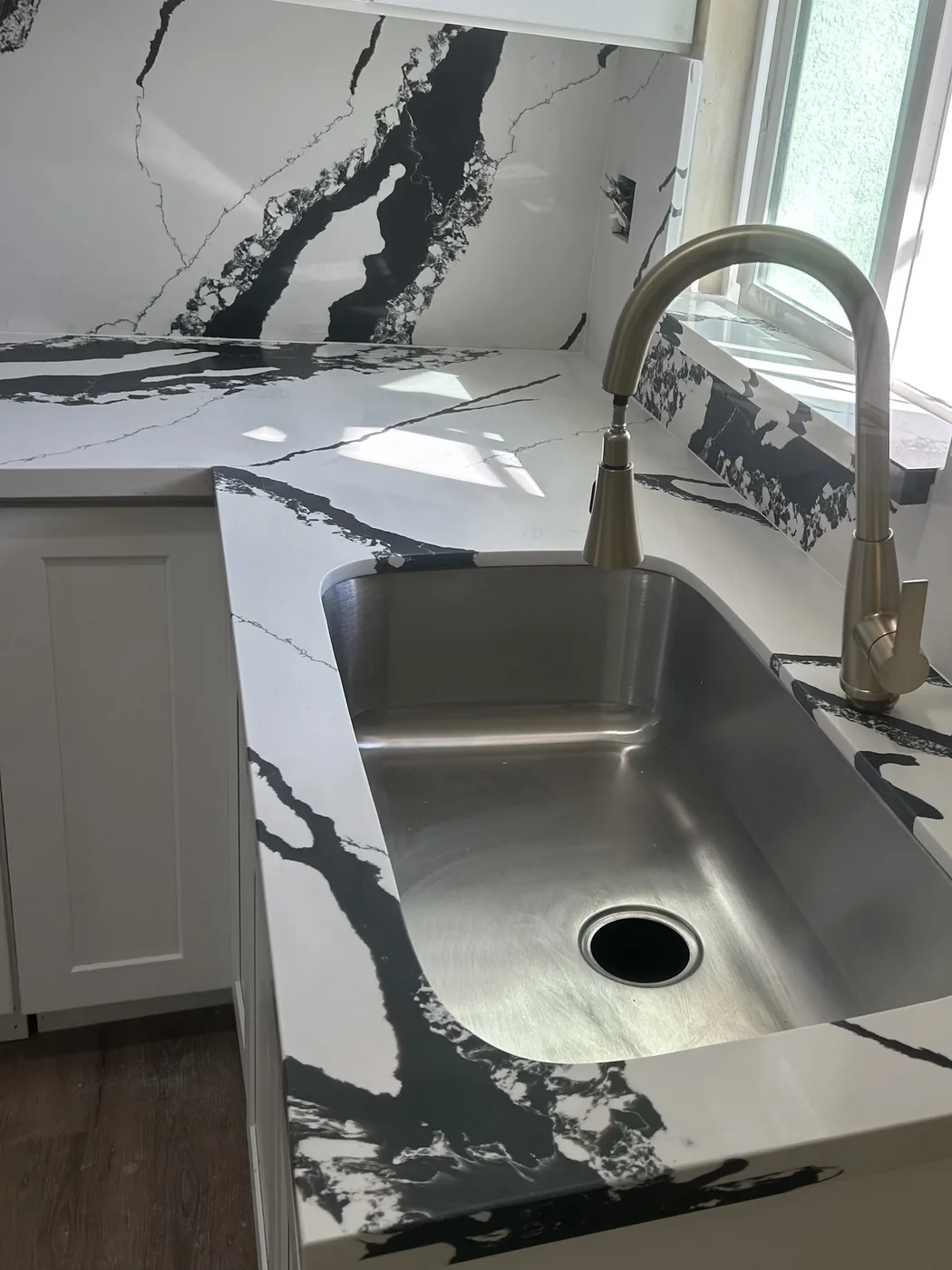 A veined black and white quartz counter with a matching slab backsplash and an undermount stainless sink